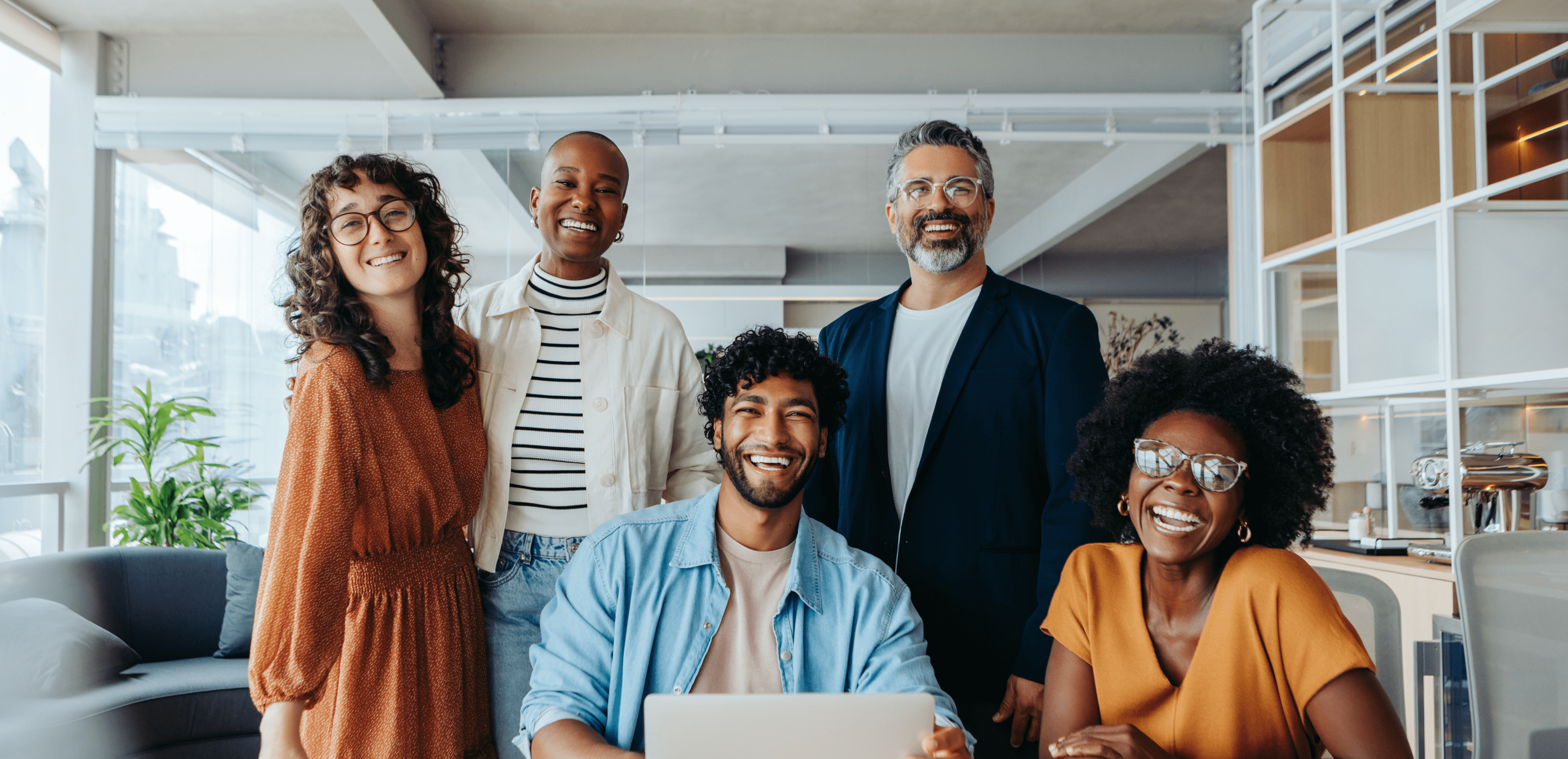 A diverse group of four smiling coworkers standing and sitting in an office.